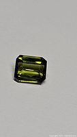 Close-up photo of the 0.87 carat green tourmaline gemstone showing octagon cut and high luster, flawless clarity visible.