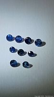 Nine natural blue sapphires with diamond cut, displayed on white background, showing varying shades of blue and faceting detail.