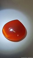 Polished pear or teardrop shaped carnelian gemstone in deep orange-red color with high gloss and translucent properties shown under light.