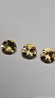 Three round golden citrine gemstones placed side by side, showing diamond cut facets and high transparency.