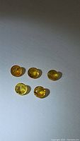 Five natural deep golden yellow sapphire gemstones on plain surface, showing round faceted oval shapes and vivid color.