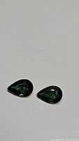 Photo of two pear-shaped green sapphires displaying consistent deep green color and clarity.