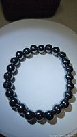Top-down view of natural hematite bead bracelet showing polished, round black metallic beads strung on elastic band.