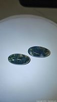 Pair of oval moss agate cabochons with green moss-like inclusions, photographed on white background under direct light showing translucency and natural patterns.