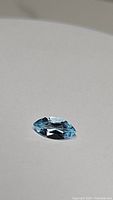 Close-up photo of a single marquis cut sky blue topaz gemstone lying flat showing facets and color tones.