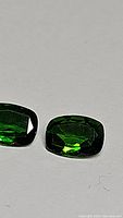 Close-up image of a pair of cushion cut green chrome diopside gemstones showing facets and color.