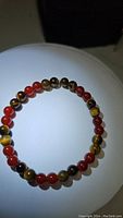 Top-down view of round polished carnelian and tiger eye bead bracelet on white surface with black background.