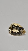 Close-up photo of a 2.71 carat pear cut natural golden citrine gemstone on white surface, showing facets and golden hue.