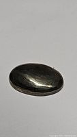 Oval cabochon cut natural pyrite gemstone with shiny golden metallic surface, showing smooth polished finish and light reflection.