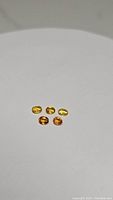 Five oval cut sapphire gemstones of canary yellow and orange colors arranged on a flat white surface.