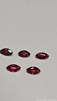 Five marquis cut hot pink natural sapphires shown on white background under even lighting.