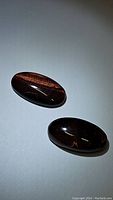Pair of polished oval cabochon red tiger's eye gemstones showing characteristic chatoyant stripes with light reflection highlighting surface and color.