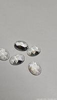 Five oval rose cut natural crystal quartz gemstones with high clarity and transparency, arranged on a plain surface.