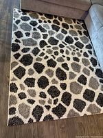 Photo showing a rectangular carpet on a floor between two couches, cream background with various sized dark and light brown spots