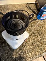 Overall image showing the black charcoal basket on top of the white electric stove with power cord.