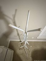 Top view of white metal coat rack showing central pole with six hooks and round white plastic tips.