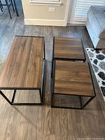 Top angle view of one rectangular and two square tables showing wood grain tops and black metal frames on wood floor.