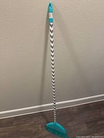 Full view of the long handle dust brush standing upright showing the chevron patterned handle and turquoise brush head.