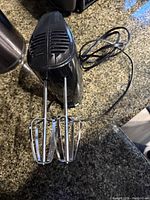 Black electric hand mixer with two metal beaters placed on kitchen countertop.