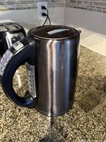 Photo showing side view of programmable electrical kettle with black handle and control buttons on handle, placed on kitchen counter.