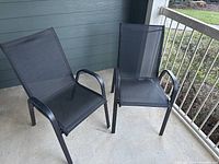 Two black heavy duty garden chairs with mesh seating and backrest, metal armrests and frames, placed outside on a porch.