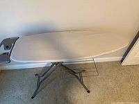 Side view of the ironing board showing the padded surface, metal frame and storage rack beneath