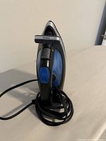 Front view of blue and black electric iron with visible blue steam button and black handle.