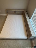 Queen-sized bed frame with light wood finish and built-in shelving headboard arranged along two wall sides, showing mattress on bed frame.