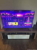 58 inch Hisense smart TV powered on, displaying a colorful cityscape image to confirm working condition. The TV is placed on a wooden TV stand with two cabinets below.