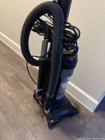 Side view of the vacuum cleaner showing cord wrapped around the handle and attached hose.