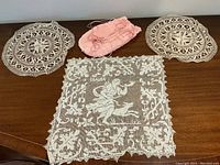 Overview of three lace doilies and pink silk pleated drawstring bag on wooden surface.