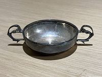 Side view showing one handle and the shallow bowl profile with a dent visible on the side.