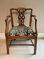 Front view of walnut armchair showing carved decorative backrest and upholstered seat.