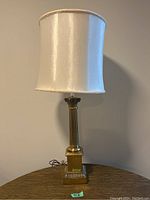 Full view of the brass table lamp with white shade on table against beige wall