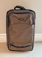 Front view of brown Briggs & Riley rolling suitcase showing front zippered compartments and black trim.