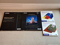 Four boxes of Epson professional photo paper on carpet: Metallic Photo Paper Glossy 17x22, Ultra Premium Photo Paper Luster 17x22, Borderless 11x14 Matte and Premium Glossy Paper boxes.