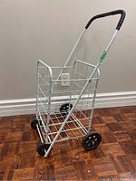 Front angled view of white metal folding shopping cart showing basket, wheels, and handle