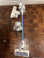 Full view of Tineco cordless vacuum cleaner including main unit, motorized brush, wall mount dock, power cord, and accessories on wooden floor.