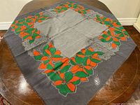 Full view of the scarf spread out, showing the two-tone grey background with a vibrant border of red and green floral motifs.