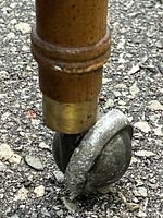 Close-up of metal caster wheel mounted on wood leg with brass sleeve showing wear