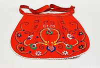 Front view of a red vintage apron with colorful floral and heart embroidery, scalloped edges with white lace trim, and fabric ties
