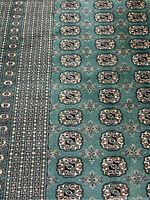 Close-up image showing part of the intricate geometric medallion pattern and border on the green Afghan Bokhara rug.