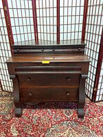 Front view of the 3-drawer antique Empire dresser against a folding screen backdrop on a patterned carpet.