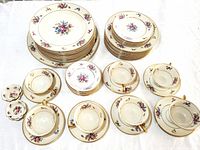 Top view showing stacks of dinner plates, salad plates, tea cups with saucers, and leaf-shaped butter pats.