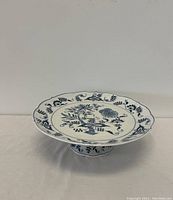 Blue Danube blue and white ceramic pedestal cake plate viewed from side angle, showing floral pattern on top and scalloped edges.