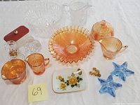 Photo shows full lot with crystal bowl, carnival glass bowls, milk glass butter box with red lid, clear glass pitcher, candle holders, floral tray, blue star-shaped glass items, and amber glass marbles.