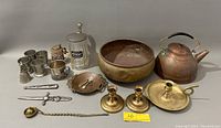 Wide view showing all metal items including tea kettle, brass bowl, candle holders, pewter cups, beer stein, spoons, dagger, and glass container.