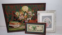 Three framed embroidered needlepoint artworks are shown together, including a floral bouquet piece, a smaller florally embroidered rectangular piece, and a floral seashell piece in a white frame.