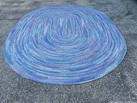 Full view of oval braided area rug laid flat on pavement showing overall shape and color.