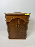 Front view of the custom-made wooden corner cupboard showing the arched double-door with handles and natural wood grain finish.